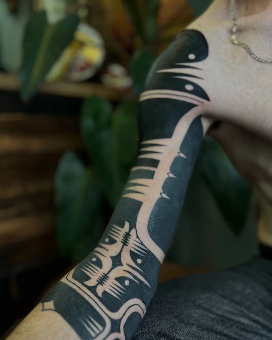 Abstract blackwork arm sleeve with sweeping solid black forms and negative-space linework.
