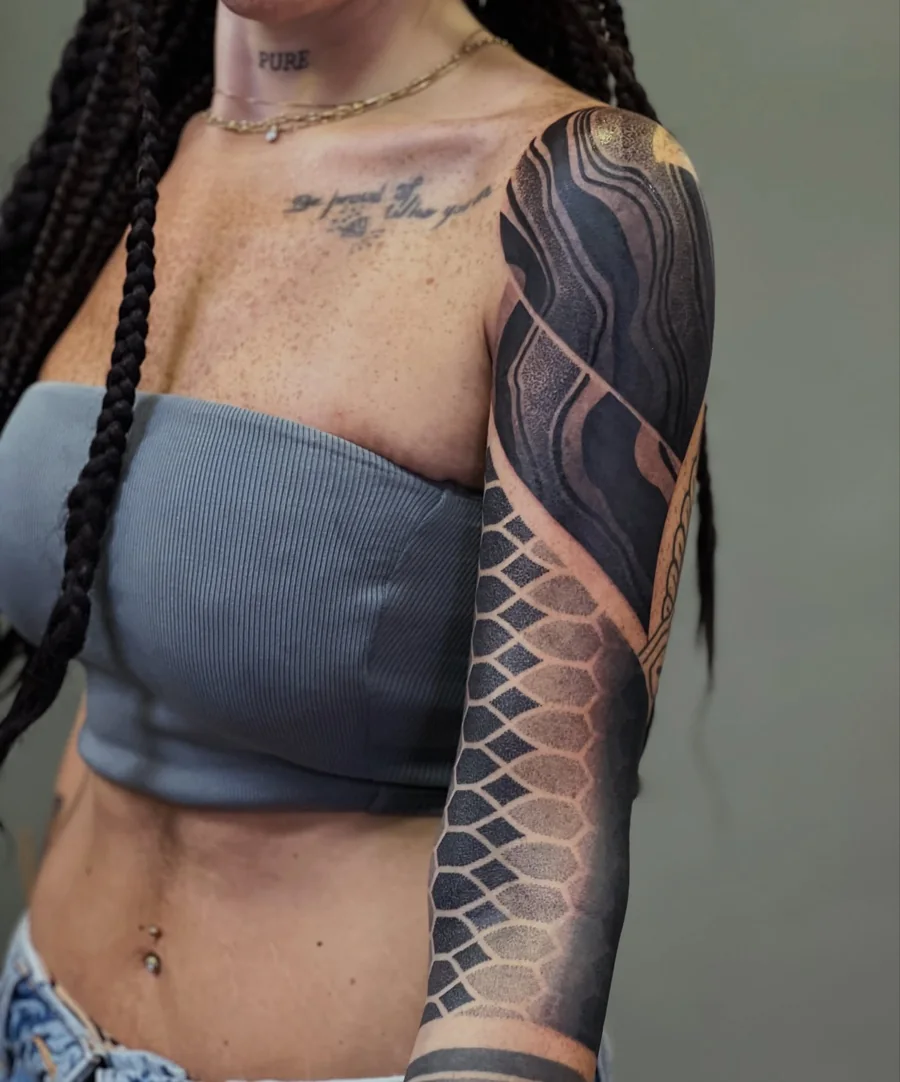 Full arm blackwork sleeve mixing large flowing black forms with a geometric lattice pattern.