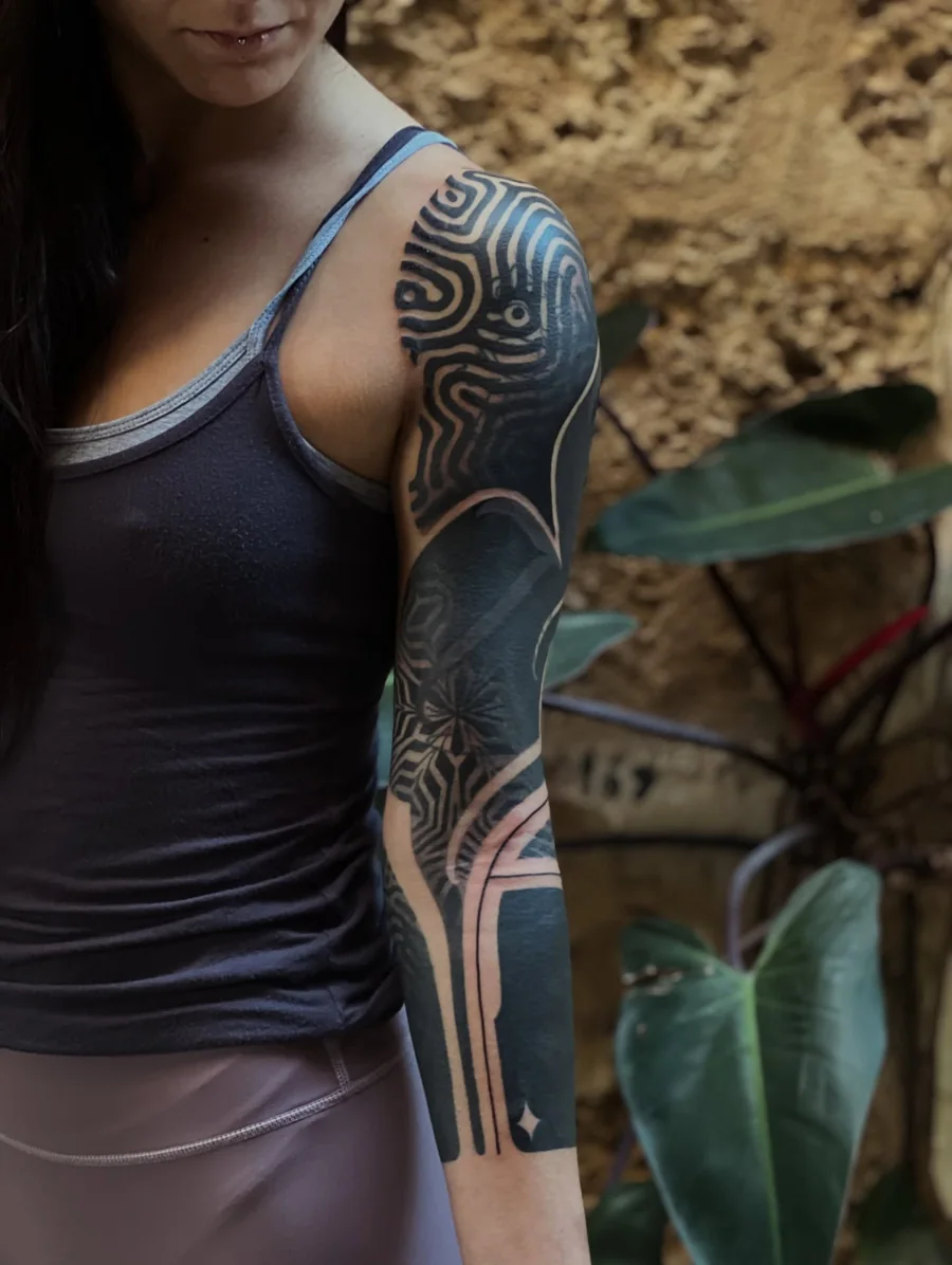 Ornamental blackwork sleeve with a maze-like shoulder pattern, flowing forms, and fine dotted textures.