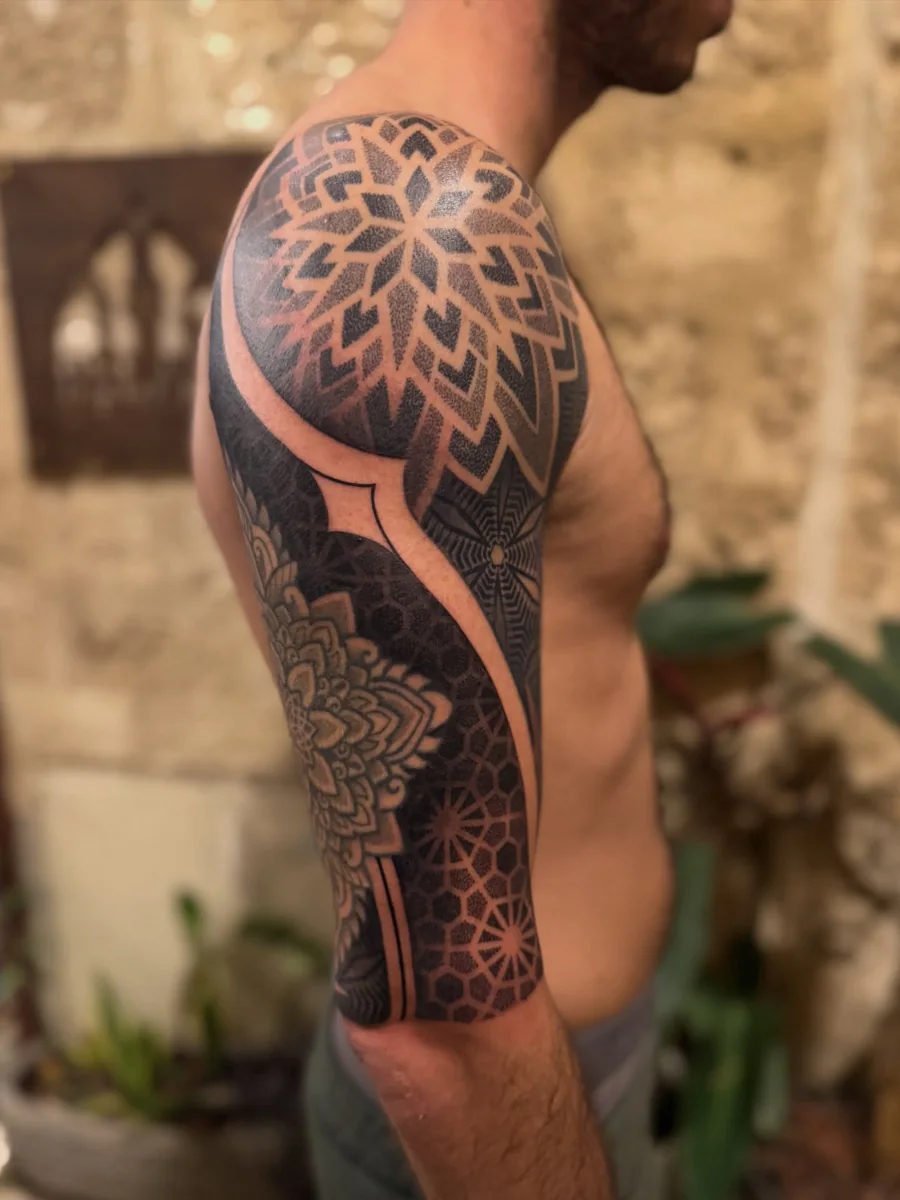 Geometric blackwork sleeve with a large floral mandala over the shoulder and a curved negative-space band.