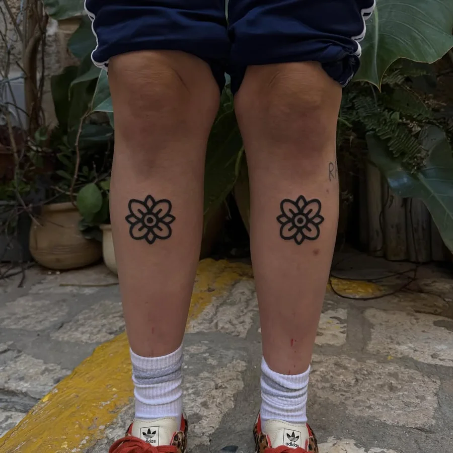 A matching pair of simple black flower tattoos, one on each knee.