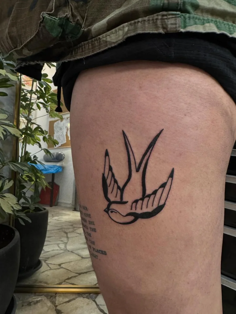 A stylized swallow tattoo in black linework on the thigh.