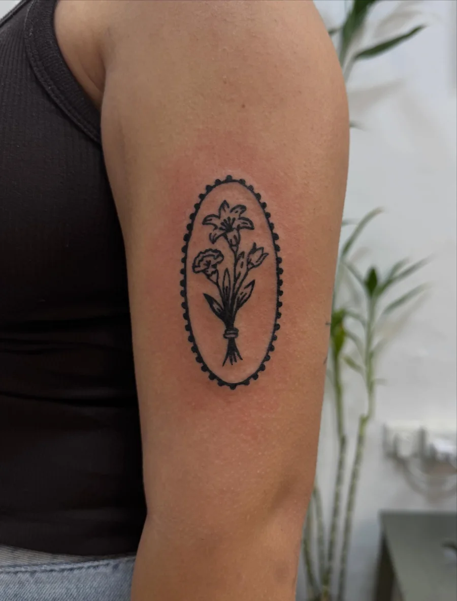A fine-line botanical bouquet within a dotted oval frame on the upper arm.