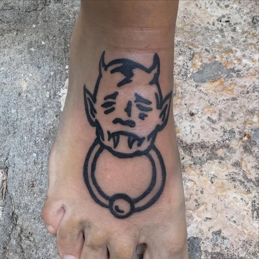 A horned face holding a ring, drawn in bold black lines on the foot.