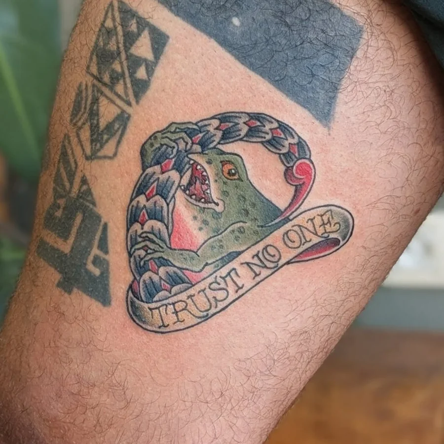 A traditional colored handshake-and-snake tattoo with the words “TRUST NO ONE” on the leg.