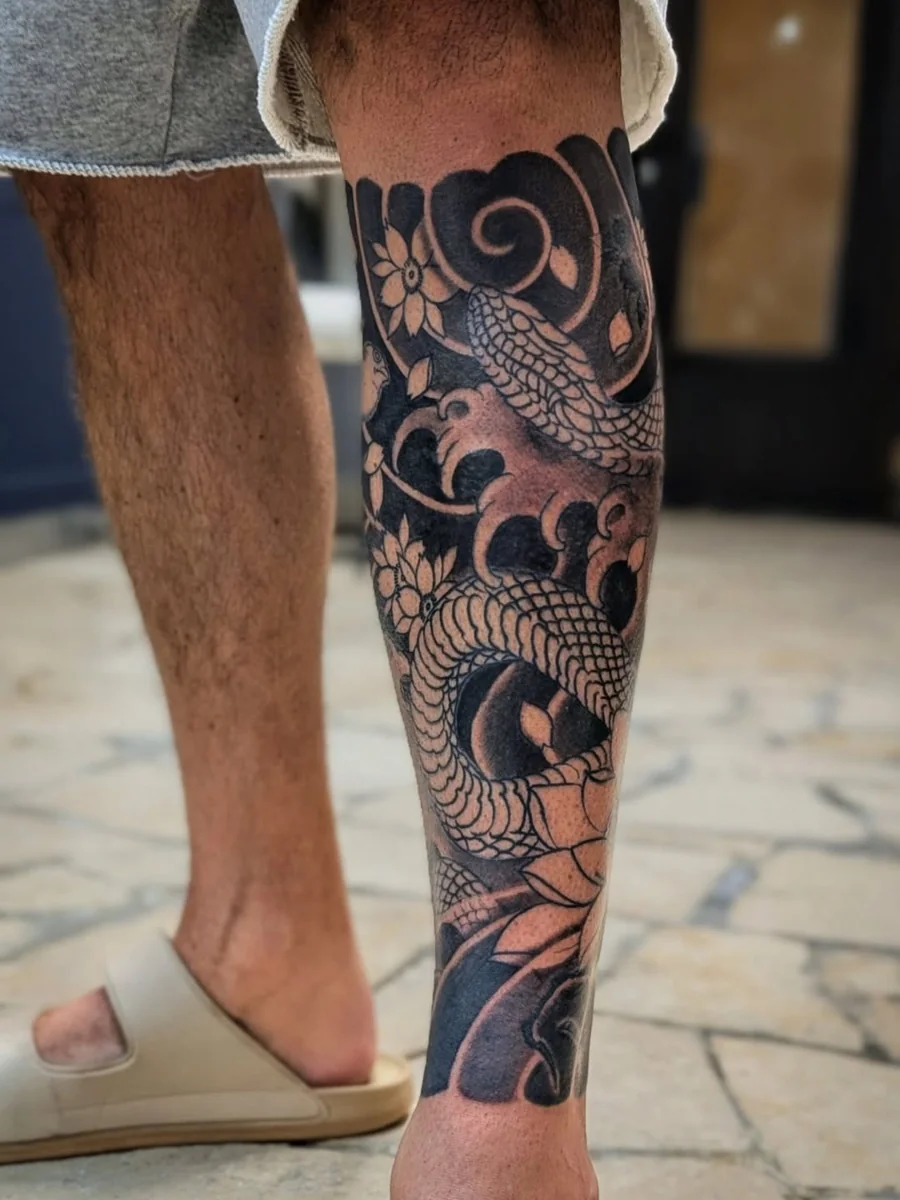 A dense Japanese-style dragon and swirling cloud tattoo in black on the lower leg.