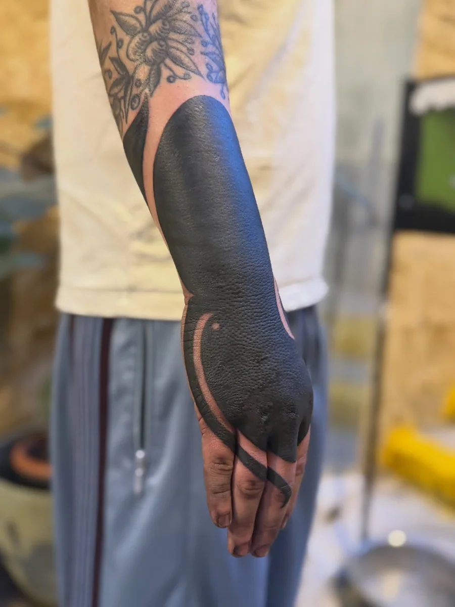 Solid black tattoo coverage across the forearm and hand by Yonatan
