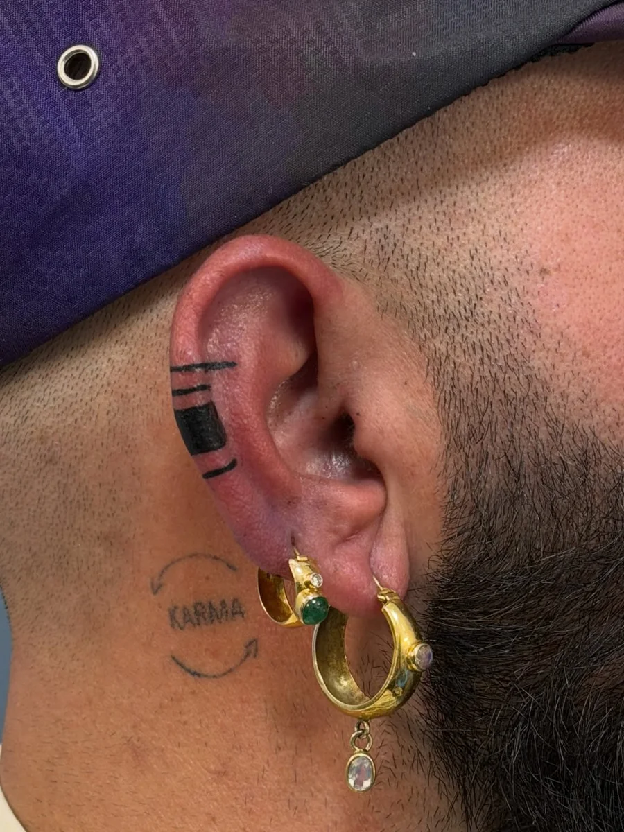 Minimal black tattoo bands across the upper ear by Yonatan