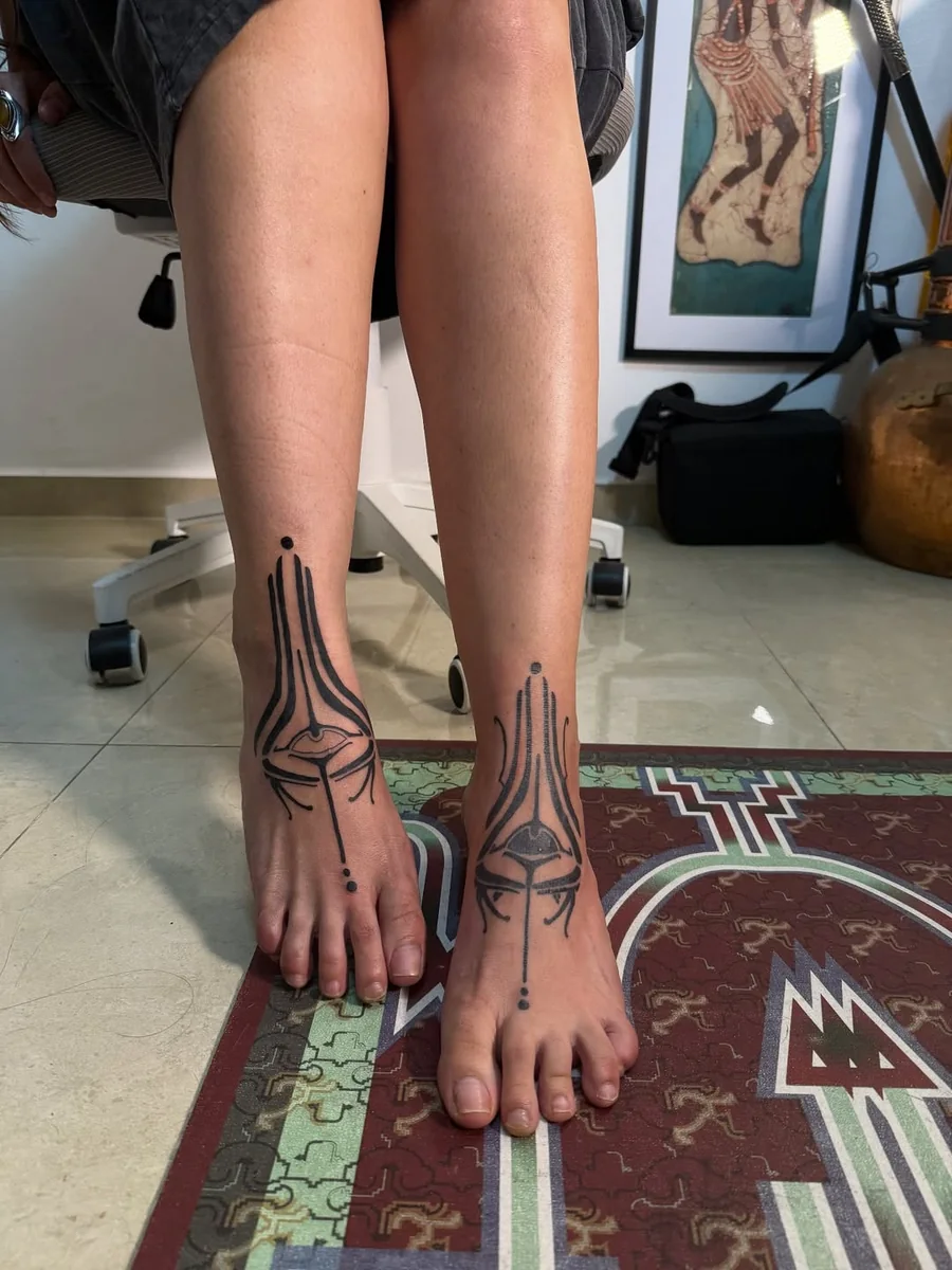 Paired tribal tattoos across the ankles and feet by Yonatan