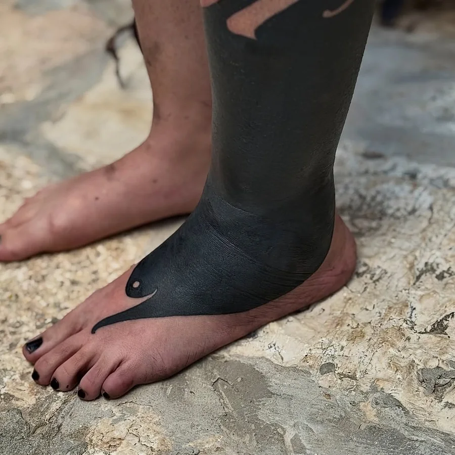 Solid black tattoo coverage extending from the lower leg onto the foot by Yonatan